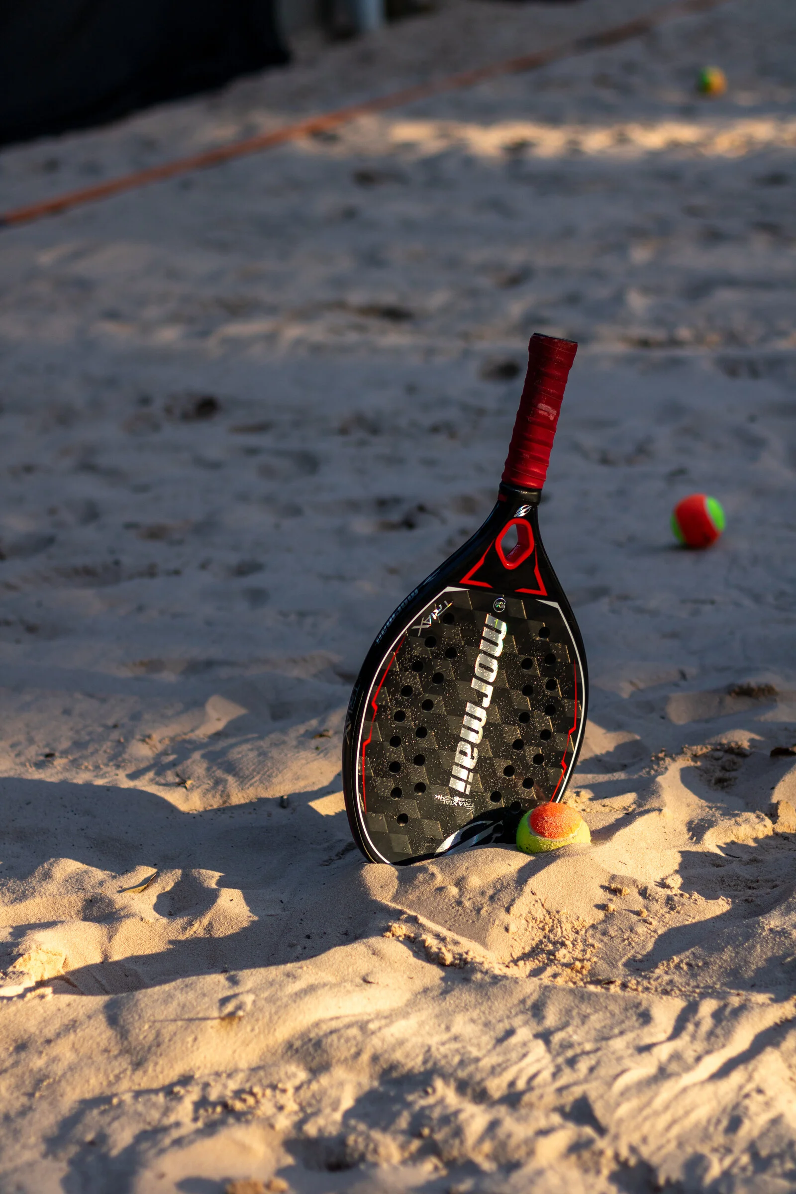 Raquete e bola de beach tennis na areia ao pôr do sol